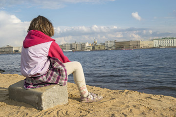 Fototapeta na wymiar Девочка сидит на пляже и смотрит вдаль