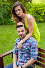 Man sitting on  bench in the garden. Girl standing behind him. Positive emotions.