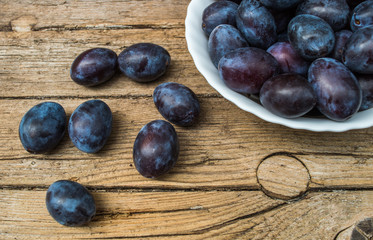 Plate full of fresh plums on a wooden background