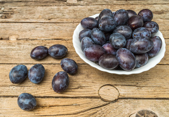 Plate full of fresh plums on a wooden background