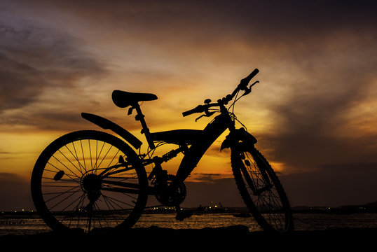 Silhouette of mountain bike parking on jetty beside sea with sun