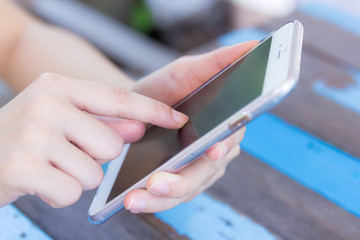 Close up of a woman using mobile smart phone on wooden table bac