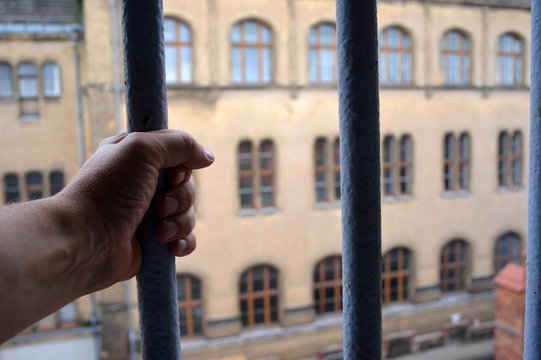 Hand on prison bars looking through a window from inside a jail 