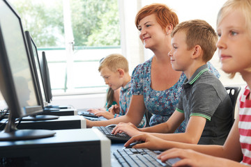 Male Elementary Pupil In Computer Class With Teacher