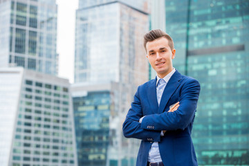 Handsome businessman in suit standing on the street in blue suit. Modern skyscrapers on the background.