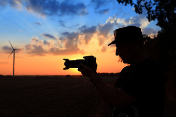Mężczyzna z aparatem na tle zachodzącego słońca. - obrazy, fototapety, plakaty