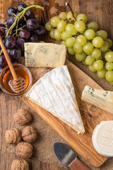 wooden board with cheeses, grapes, nuts and honey