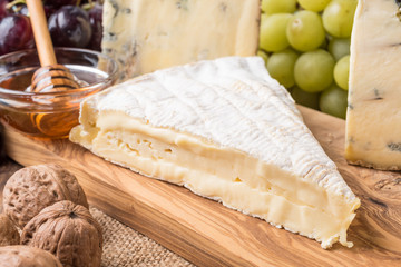 wooden board with cheeses, grapes, nuts and honey