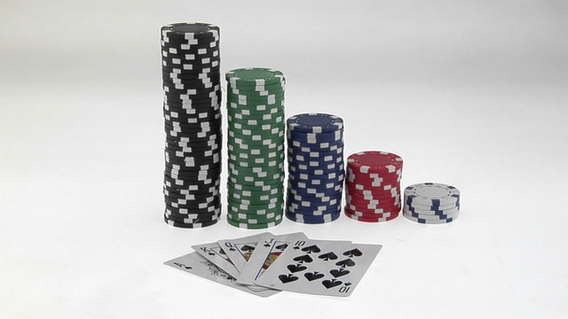 Stacks of poker chips sit in a row, arranged by value behind a deck of playing cards.