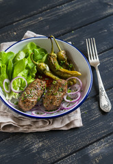 lamb kebab, spicy roasted peppers and fresh green salad on the blue plate on a dark wooden surface, healthy lunch