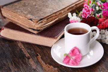 Old books with beautiful flowers and cup of tea on wooden table close up