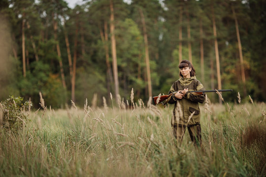Young beautiful woman hunter with a shotgun in the forest
