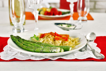 Roasted asparagus and tasty pasta with vegetables on plate on wooden table background