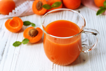 Cup of apricot juice and fresh fruits on table close up