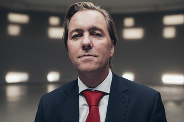Arrogant entrepreneur wearing suit with red tie in empty room.