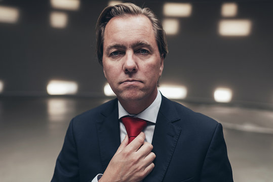 Arrogant entrepreneur wearing suit with red tie in empty room.
