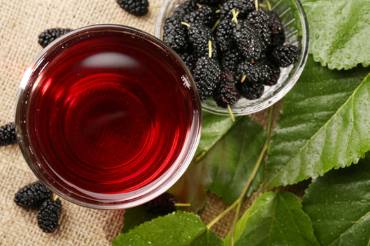 Glass of refreshing mulberry juice with berries on table close up