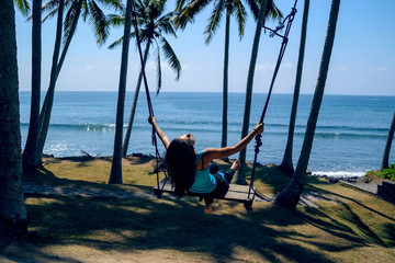 Girl on a swing on the beach with beautiful view on palms and ocean, Indonesia