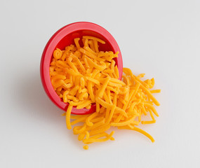 Bowl of shredded sharp cheddar cheese spilling on cutting board