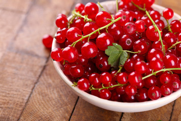Fresh red currants in bowl on wooden table close up