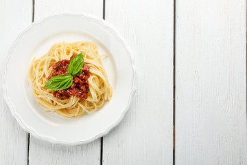 Spaghetti Bolognese on white plate, on color wooden background