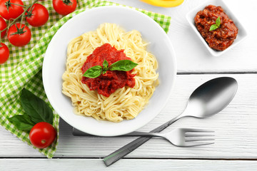 Spaghetti with tomato sauce and cheese on white plate, on color wooden background