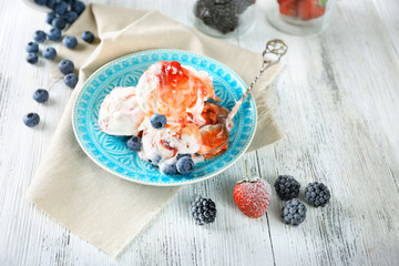 Delicious ice cream with fresh frozen berries and sauce, on color wooden background