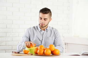 Young man using citrus-fruit squeezer, preparing orange juice