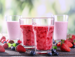 Glasses of berry smoothie on wooden table on blurred background