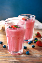 Glasses of berry smoothie on wooden table on dark background