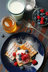 Sweet homemade waffles with forest berries and cream on plate, on dark wooden background