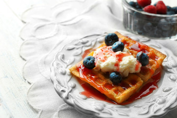 Sweet homemade waffles with forest berries on plate, on light background