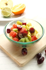 Fruit salad in glass bowl, on light wooden background