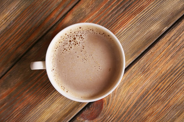 Cup of coffee with foam on wooden table, top view