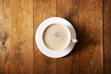 Cup of coffee with foam on wooden table, top view