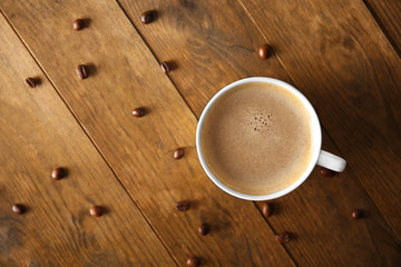 Cup of coffee with beans on wooden table, top view
