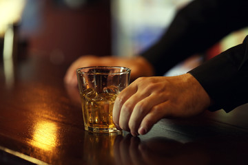 Whiskey glass tumbler in male hand on bar counter