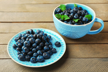 Cup and plate with fresh blueberries on wooden table close up