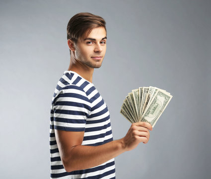 Handsome young man holding money on gray background