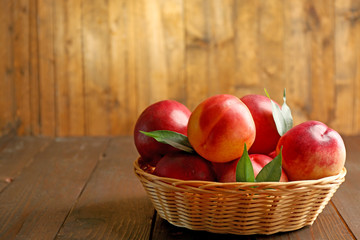 Fresh peaches in wicker basket on wooden background