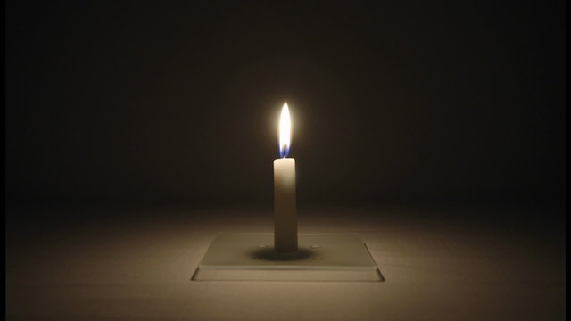 A small candle burns in a dark room.