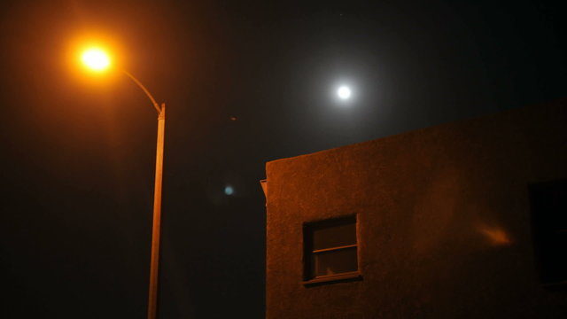Time lapse of moon rising over a house and street lamp.