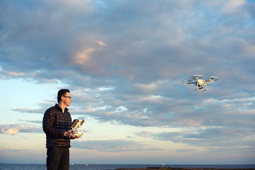 man flying drone with remote control at the beach at sunset golden hour