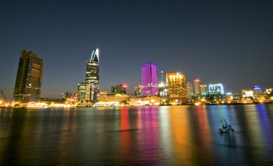 Cityscape of Ho Chi Minh at night with bright illumination of modern architecture, viewed over Saigon river in Southern Vietnam.