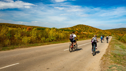 Group of cyclists on road stretches into the distance on the background of bright autumn trees on a hill. Russia