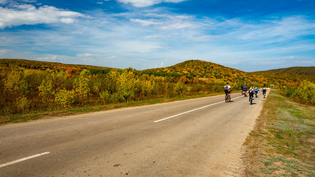 Group of cyclists on road stretches into the distance on the background of bright autumn trees on a hill. Russia