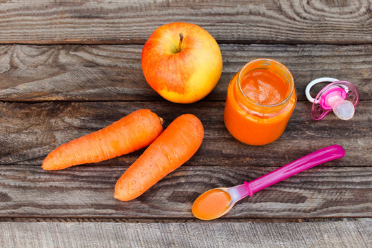 Fruit puree, carrot, apple and pacifier on wooden background