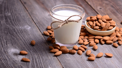 Almond milk in glass with almonds in bowl, on wooden background