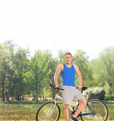 Young cyclist posing with his bicycle by a pond