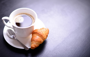 Croissant and cup of coffee on black background